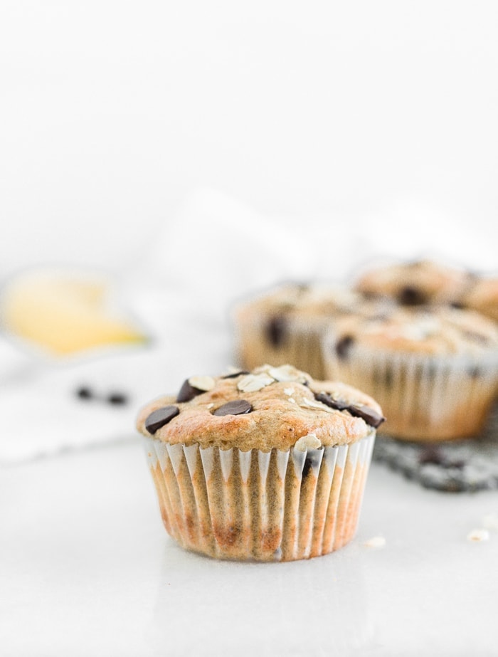 Healthy banana chocolate chip blender muffin up close with banana and more muffins behind it.