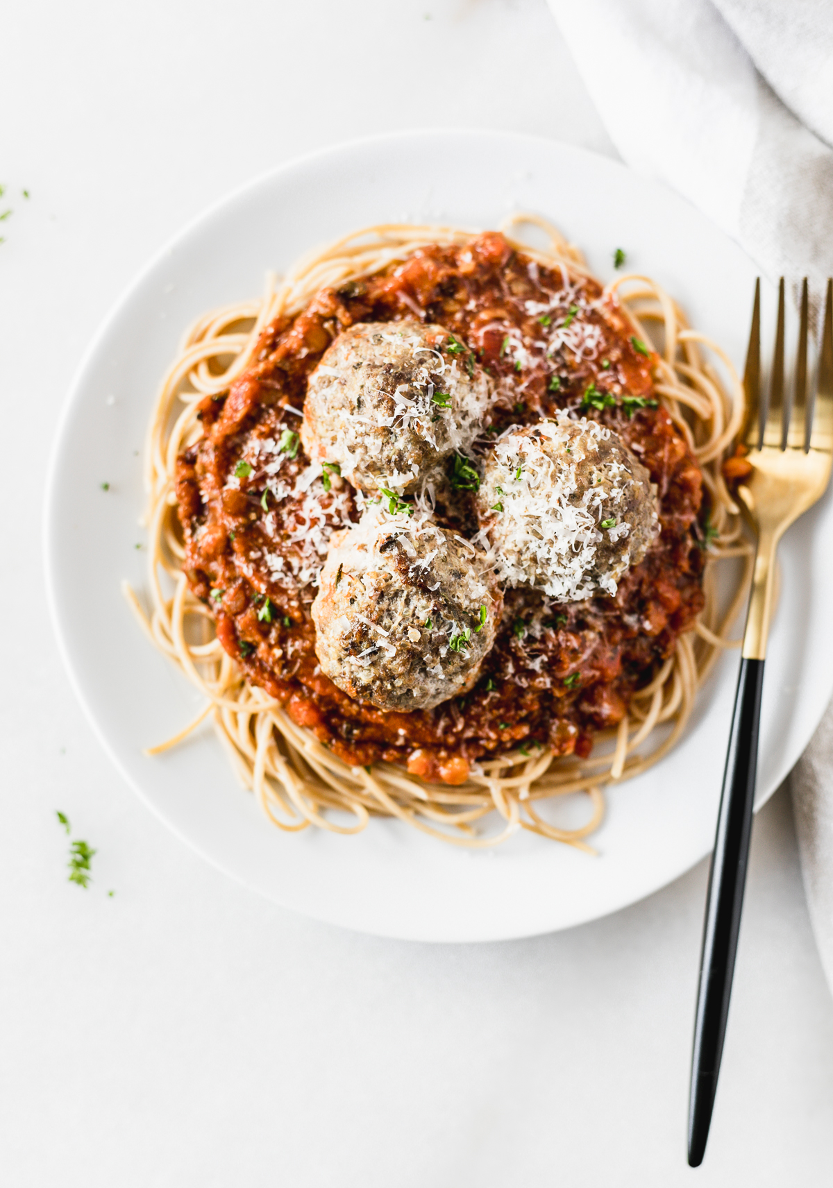 overhead view of a plate of spaghetti with three beef and quinoa meatballs sprinkled with cheese and parsley with a black and gold fork.