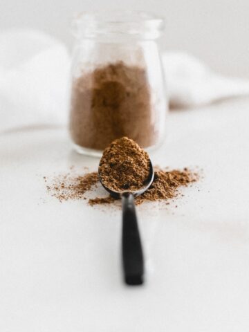 homemade chai spice blend on a black spoon with more in a clear container behind it.