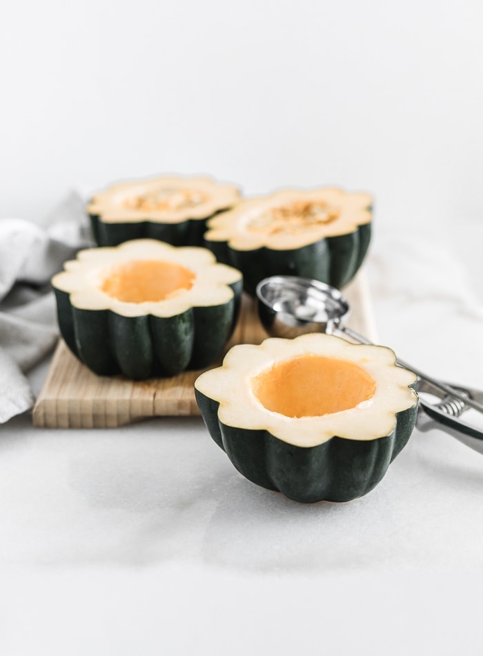 acorn squash halves on a cutting board with a scoop next to them.