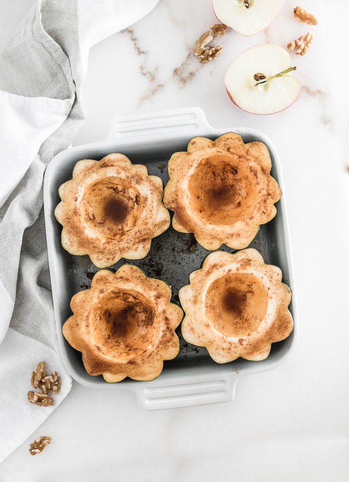 overhead view of 4 acorn squash halves in a white square baking dish sprinkled with cinnamon and maple syrup.