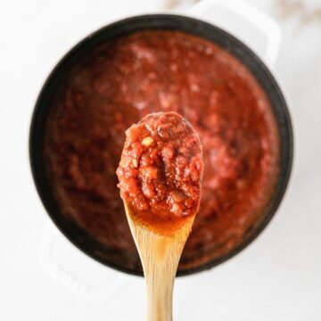 wooden spoon of easy spaghetti sauce over a white pot of sauce.