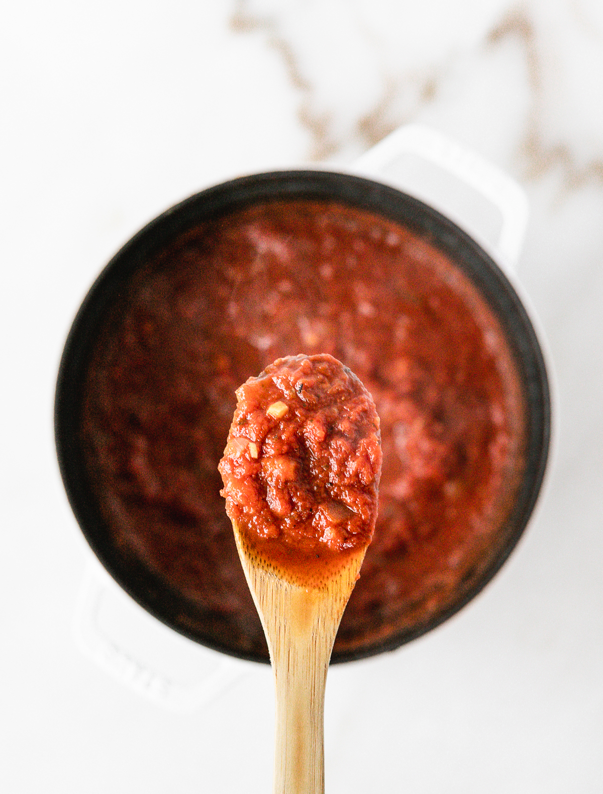 wooden spoonful of homemade spaghetti sauce over a white pot of sauce.