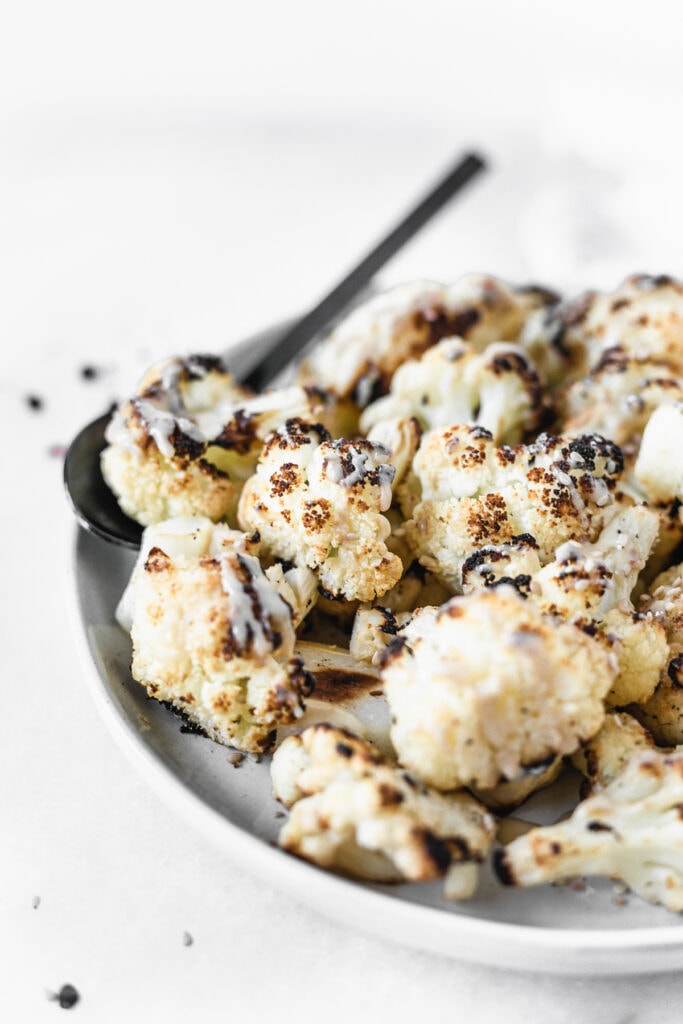 tahini roasted cauliflower drizzled with tahini on a grey plate.