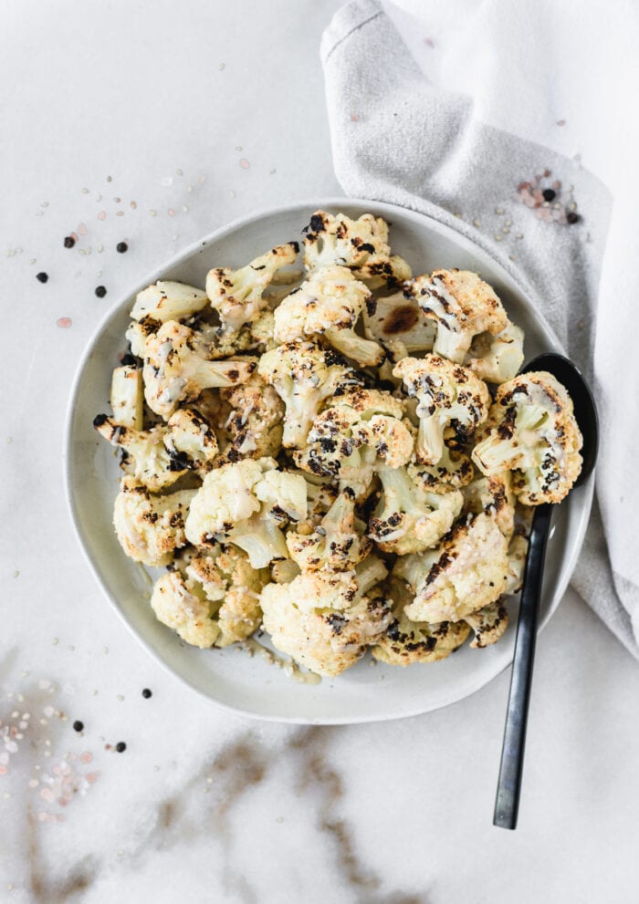 overhead view of tahini roasted cauliflower with tahini drizzle on a grey plate with a black spoon in it.