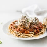plate of spaghetti with three beef and quinoa meatballs sprinkled with cheese and parsley.