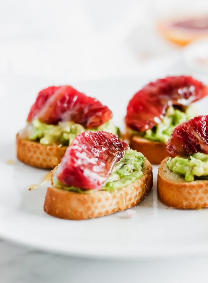 Close up view of four blood orange avocado crostini on a white serving plate.