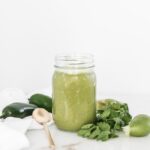 green enchilada sauce in a jar surrounded by peppers, limes and cilantro.