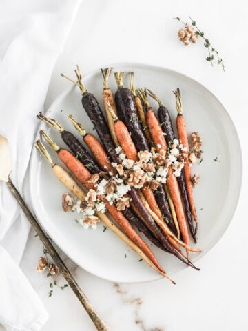 Overhead view of maple dijon roasted carrots with goat cheese, walnuts and thyme on a white plate.