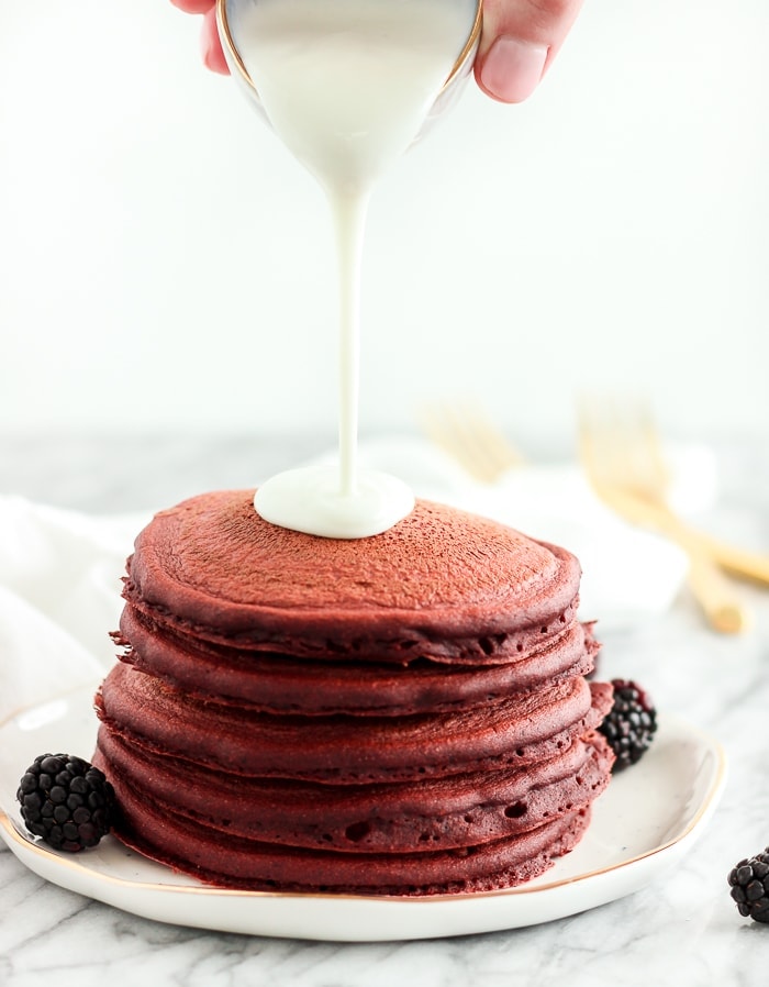 healthy red velvet pancakes with cream cheese glaze being poured over the top