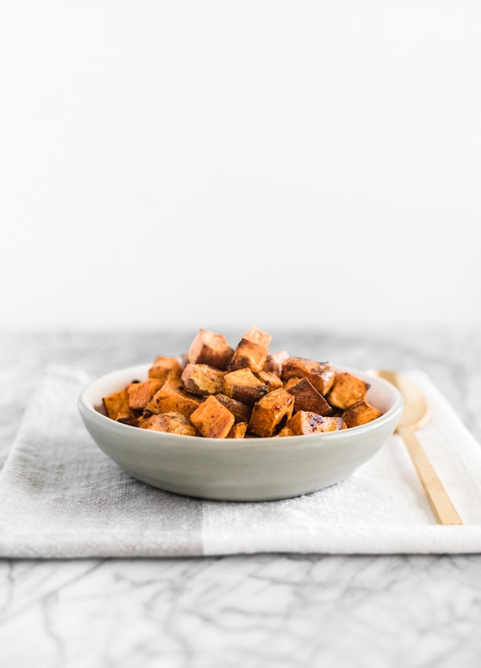 simple roasted sweet potatoes in a grey bowl with a gold spoon next to it.