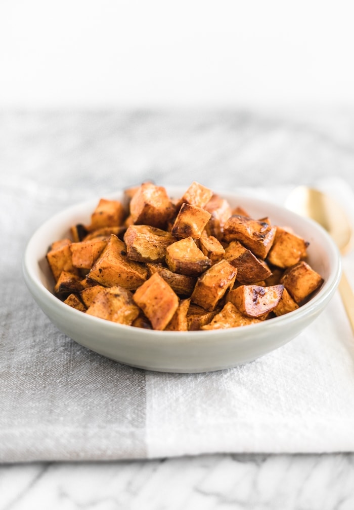 simple roasted sweet potato cubes in a white bowl on top of a folded grey and white napkin.