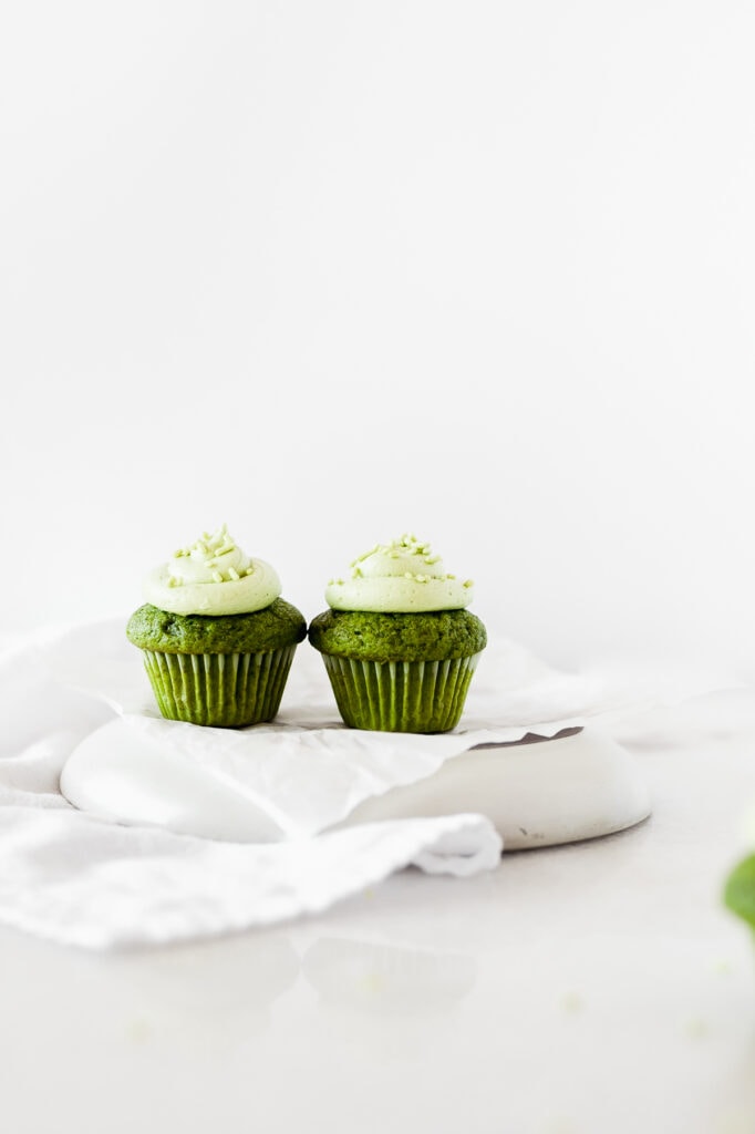 two mini matcha cupcakes side by side on a white platter with a white napkin next to it.