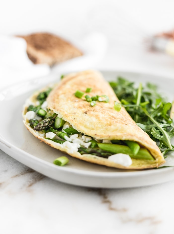 closeup of asparagus and goat cheese omelette with extra asparagus next to it on a white plate.