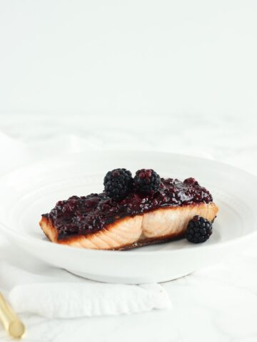 blackberry glazed salmon on a white plate with a white napkin underneath.