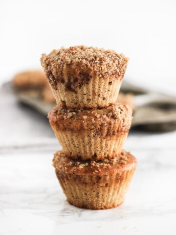 close up of three buttermilk spice muffins stacked on top of one another and a muffin pan behind it.