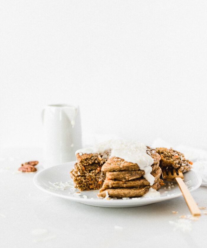 stack of carrot cake pancakes on a white plate with a bite taken out.