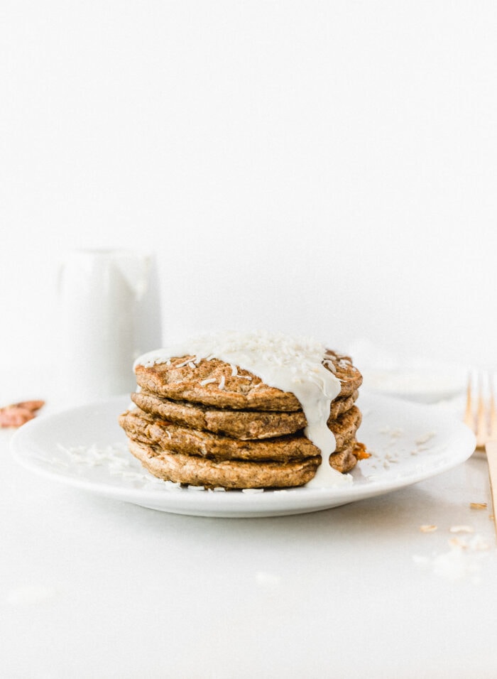 stack of healthy carrot cake pancakes with lightened up cream cheese frosting on a white plate.