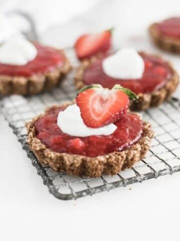 mini strawberry rhubarb tarts topped with whipped cream on a cooling rack.