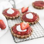 mini strawberry rhubarb tarts with whipped cream on top on a cooling rack.