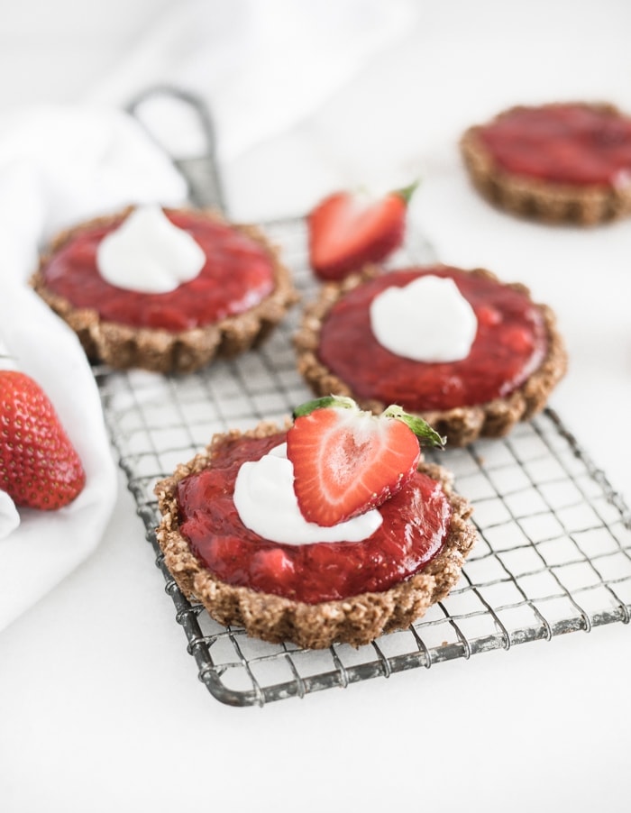 mini strawberry rhubarb tarts with whipped cream on top on a cooling rack.