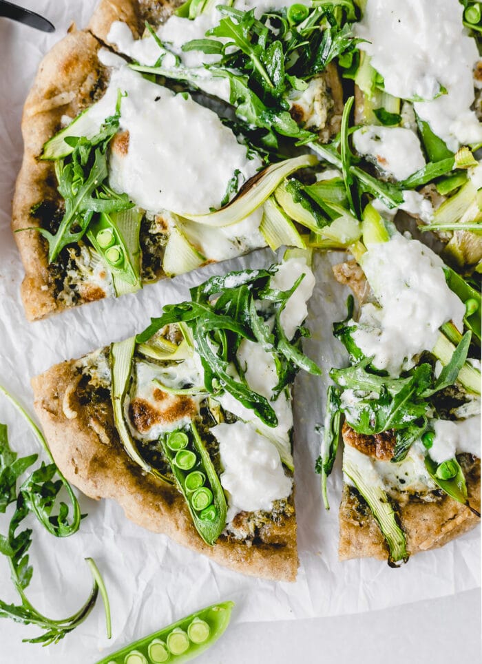 overhead view of sliced asparagus snap pea pizza with burrata and arugula.