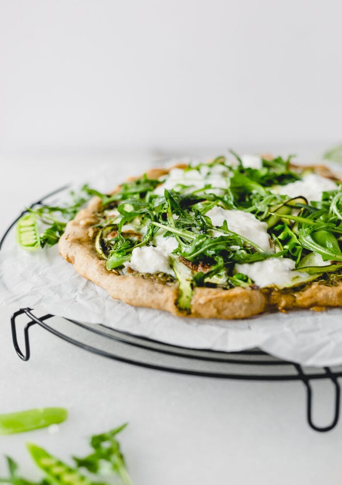 asparagus snap pea pizza with burrata and arugula on a wire cooling rack lined with parchment.