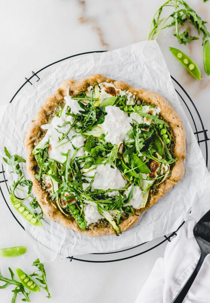 overhead view of asparagus snap pea pizza with burrata and arugula on a wire cooling rack lined with parchment.