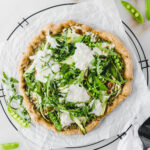 overhead view of asparagus snap pea pizza with burrata and arugula on parchment paper on a wire cooling rack.