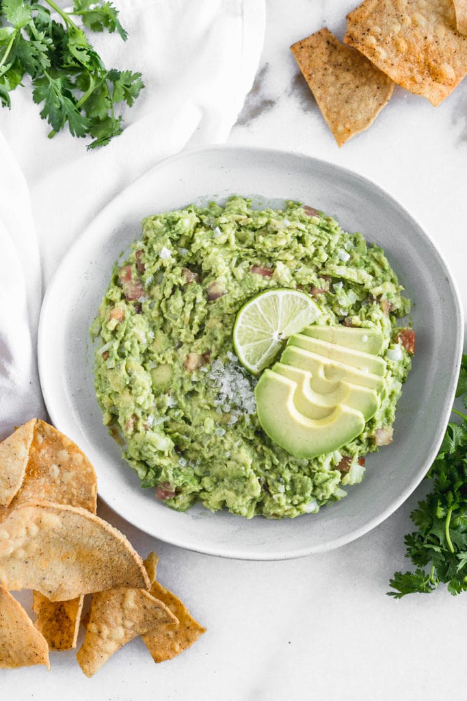 simple guacamole in a bowl with chips around it.