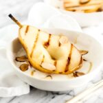 closeup of grilled pears with honey whipped ricotta and almonds in white bowls.