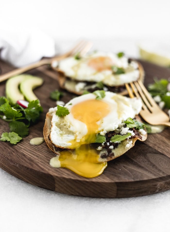 closeup of healthy huevos rancheros tostadas on a wooden serving tray with a dripping egg yolk..
