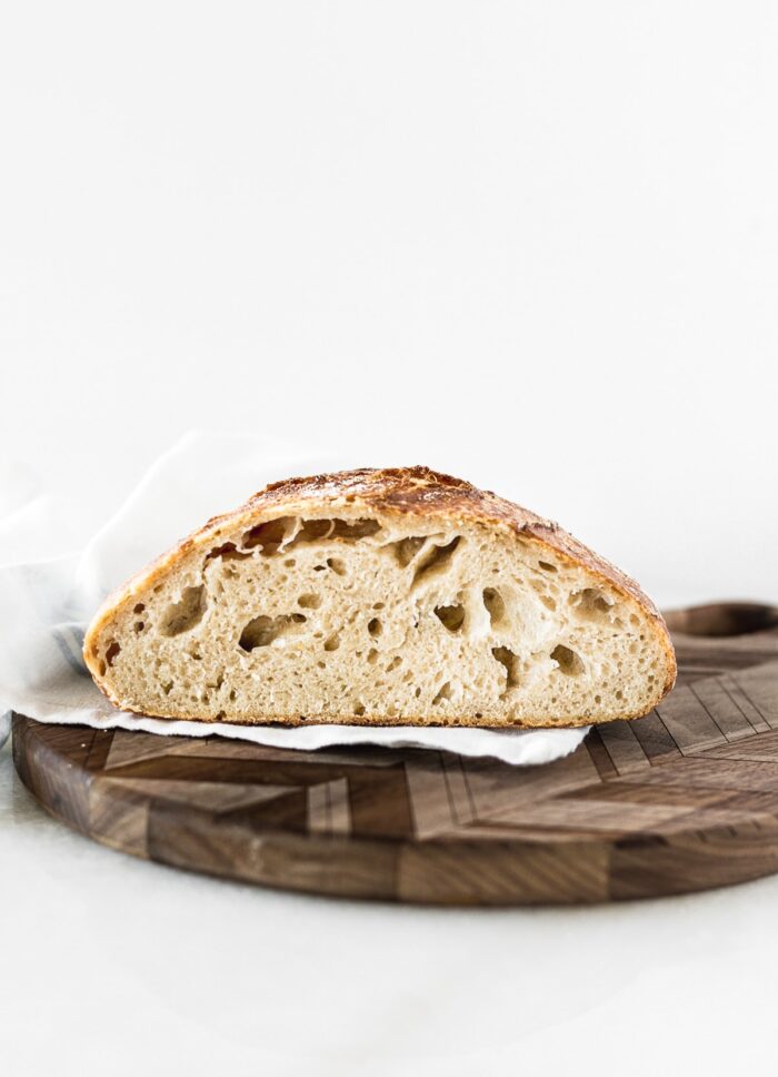 loaf of sourdough bread cut in half on a round wooden cutting board.