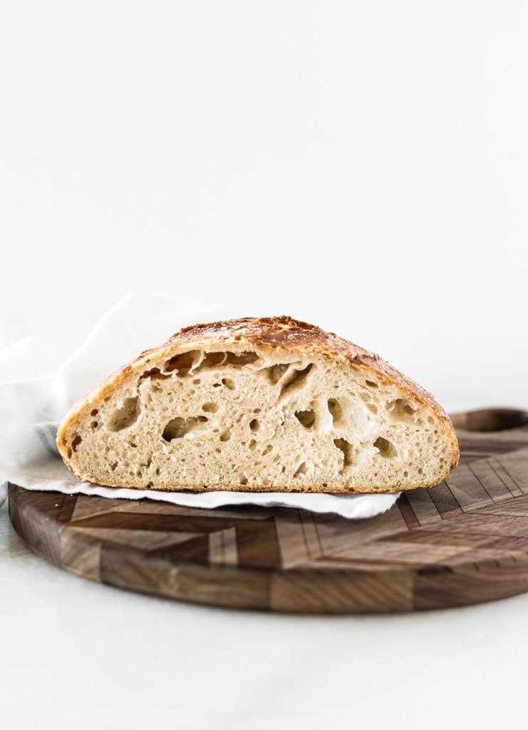 loaf of sourdough bread cut in half on a round wooden cutting board.