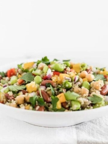 three bean quinoa salad in a white bowl on top of a white and gray napkin.
