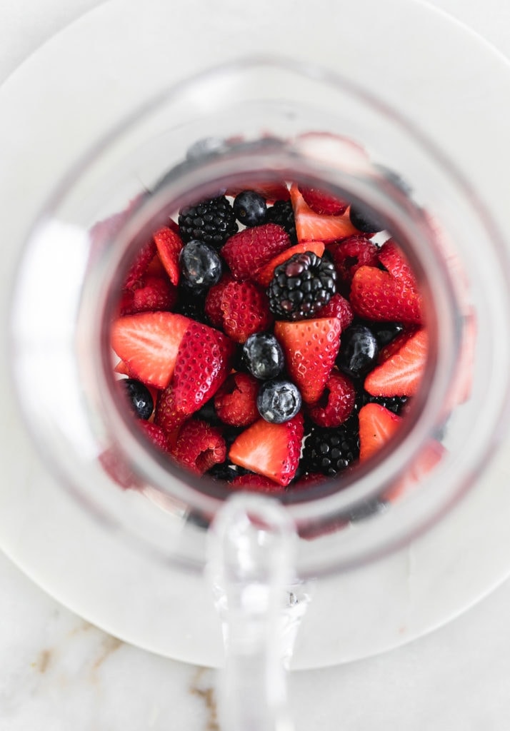Blueberries, blackberries, raspberries, and cut up strawberries at the bottom of a pitcher.