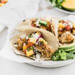 crunchy coconut fish tacos topped with a fresh mango salsa on a white plate.