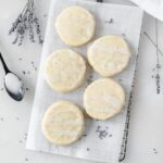 overhead view of lavender shortbread cookies on a wire cooling rack surrounded by dried lavender and a spoonful of lavender glaze.