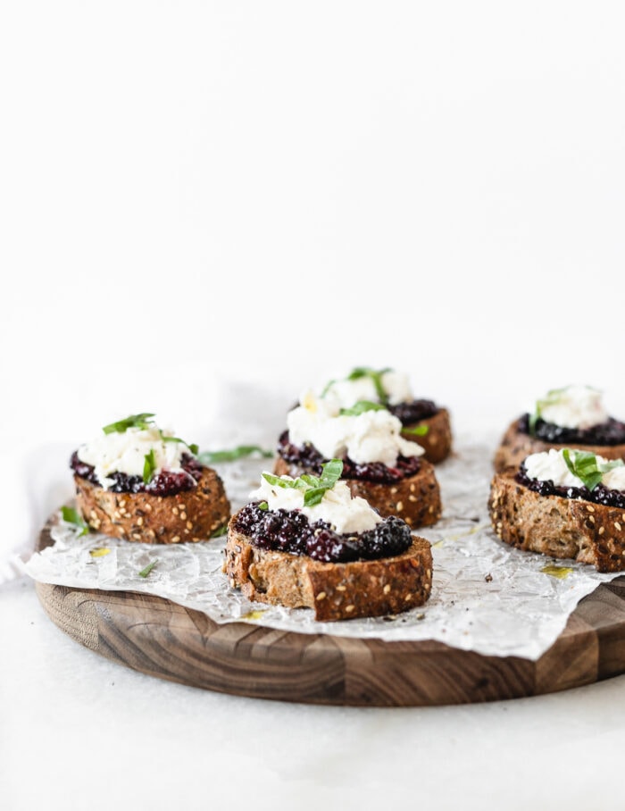 roasted blackberry burrata bruschetta on a wooden serving board covered with parchment.