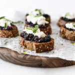 roasted berry burrata bruschetta on a wooden serving tray.