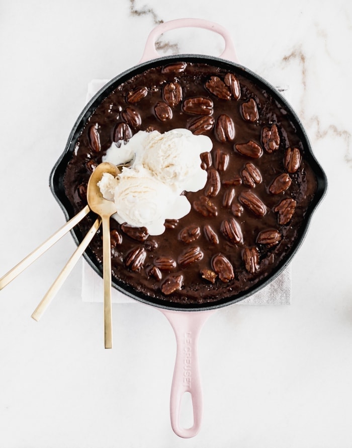 overhead view of skillet texas sheet cake with ice cream on top and three gold spoons in it.