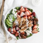 Top view of strawberry avocado salad with grilled chicken in a white bowl and a white napkin beside it.