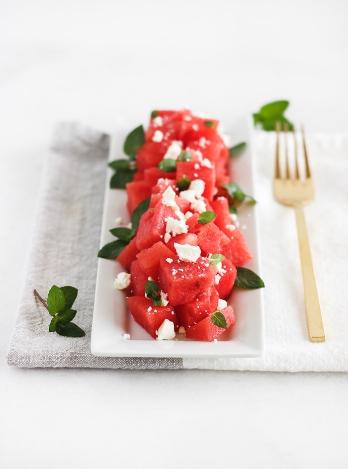 watermelon feta mint salad on a white plate with a gold fork next to it.