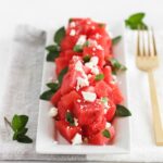 watermelon feta mint salad on a white rectangular platter with a gold fork beside it.