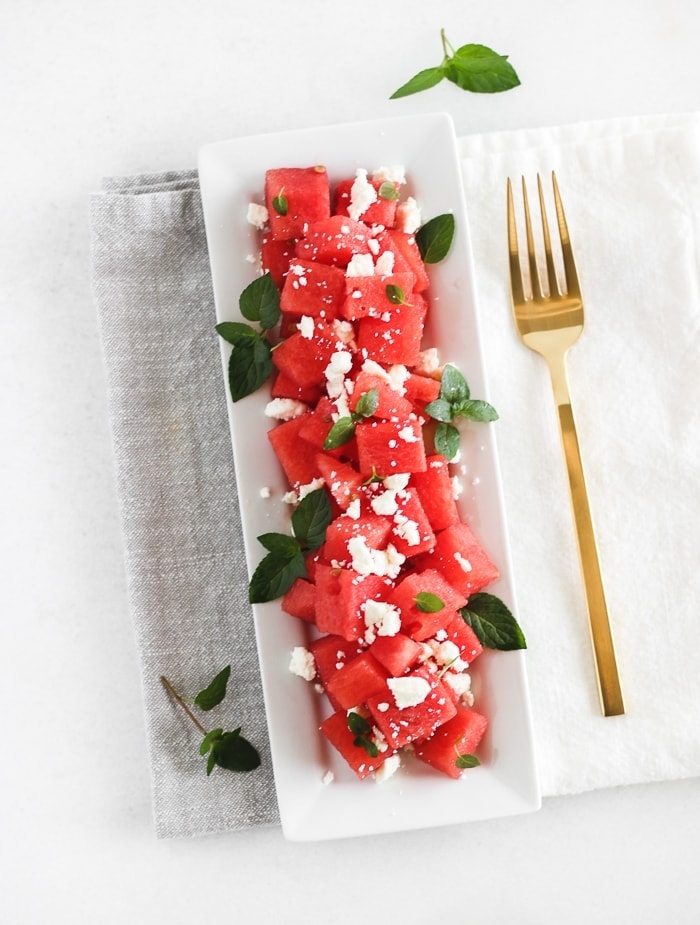 overhead view of watermelon feta mint salad on a white plate with a gold fork next to it.