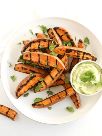 overhead view of grilled sweet potato wedges on a white plate with avocado cream sauce.