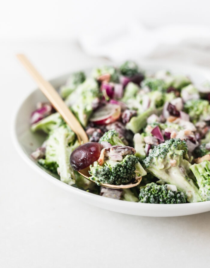 Closeup of Healthy No-Mayo Broccoli Salad in a white bowl with a gold spoon in it.