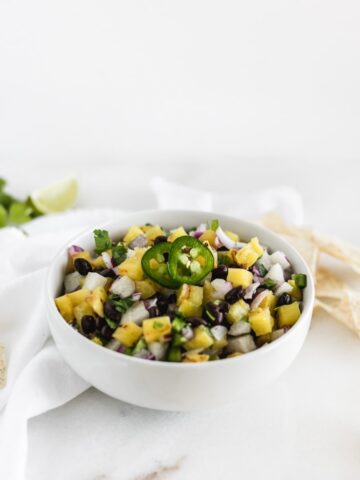 grilled pineapple black bean jicama salsa in a white bowl with a white napkin behind it.
