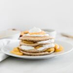 stack of healthy peaches and cream pancakes layered with yogurt and peach compote on a white plate.