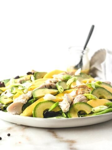 mango avocado and roasted chicken salad on a grey plate beside a black fork and white napkin.